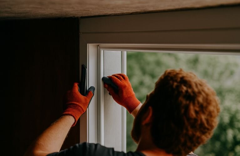 Ein Handwerker befestigt die Dichtung beim Einbau eines Kellerfensters